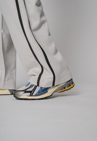 Sportliche Sneakers mit einem metallisch silber-blauen Design, einem strukturierten Obermaterial und einer dicken Gummisohle. Kombiniert mit grauen Jogginghosen mit schwarzen Streifen.