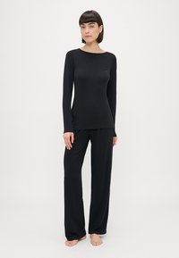 Melna garām piedurknēm apģērba augšdaļa un brīva piegriezuma bikses, kas izgatavotas no mīkstas auduma. Komplektā ir apaļa apkakle un minimālisma dizains, bez redzamām rakstajām debesīm.