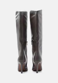 Καφέ δερμάτινες μπότες μέχρι το γόνατο με κομψό σχέδιο, μυτερή μύτη και ψηλό στιλέτο τακούνι; διαθέτουν πλαϊνούς φερμουάρ για ευκολία στην τοποθέτησή τους.