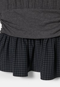 Temno siva tkanina zgoraj z nabrano, zloženo spodnjo obrobo nad mornarsko modro in sivo karirasto detajlno krilo.