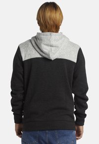 Sweat à capuche noir et gris avec un design bicolore. Tissu doux et texturé, avec une capuche et un empiècement gris, des poignets côtelés et un ourlet.