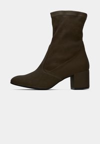 Botte de cheville marron foncé en daim avec un design ajusté, bout pointu et un talon carré épais. Texture lisse sans motifs visibles.