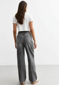 Jeans de pierna ancha, de color gris deslavado, con una cintura alta y parte trasera elástica. Combinados con una blusa corta de manga corta blanca. Tejido suave.