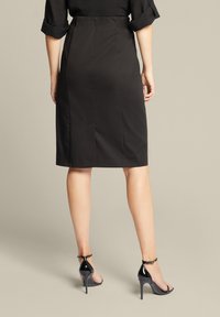 Schwarzer Bleistiftrock mit glatter Textur, knielanges Design und taillierter Silhouette. Kombiniert mit glänzenden schwarzen High Heels mit Knöchelriemen.