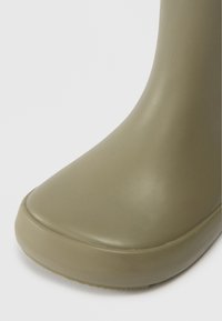 Close-up van de matte olijfgroene rubberen laarzenneus met een gladde, naadloze constructie op een witte achtergrond.