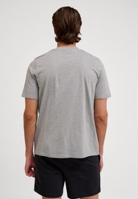 Grå t-shirt med korte ærmer lavet af bomuld, med rund hals og en afslappet pasform, vist fra ryggen, sammen med sorte shorts.