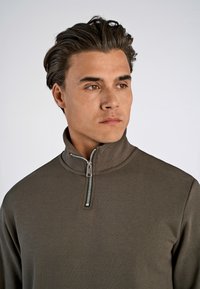 Brown zip-up sweatshirt with a high collar and silver zipper detail. Smooth, lightweight fabric with a fitted silhouette.