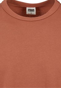 T-shirt marron en coton bio avec col rond et étiquette indiquant la marque Urban Classics, taille moyenne, fabriqué au Bangladesh.