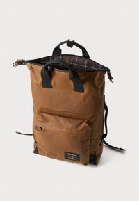 Barna viaszolt vászon hátizsák állítható fekete pántokkal, felül cipzárral záródik, elülső zsebe van, és kockás bélés található benne. Bőr kiegészítők jellemzik.