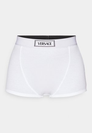Baltas kokvilnas bokseris ar melnu elastīgu jostu, uz kuras ir "VERSACE" logo. Gluda tekstūra, minimālistisks dizains un pieguļošs siluets.