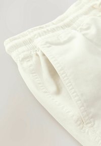 Shorts extensibles couleur crème avec une ceinture élastique et des poches latérales, présentant une texture lisse et des détails de couture soignés.