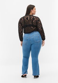 Top negro de encaje de manga larga con un cuello alto y un detalle en forma de llave, acompañado de jeans acampanados de color azul claro que cuentan con bolsillos traseros y un acabado desgastado.