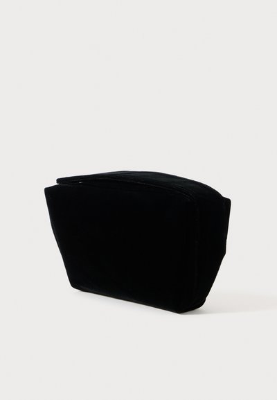 Μαύρη βελούδινη τσάντα με μαλακή υφή, τραπεζοειδές σχήμα, φερμουάρ στην κορυφή και χωρίς ορατά σχέδια ή αξεσουάρ.
