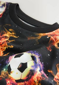 Černá tkanina s grafikou hořícího fotbalového míče a ribbed límcem u krku na oděvu.