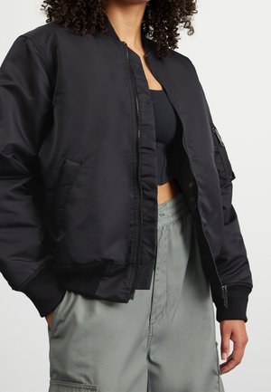 Schwarze Bomberjacke mit Reißverschluss, gerippten Bündchen und seitlichen Taschen. Aus glattem Material mit einem leicht schimmernden Finish.