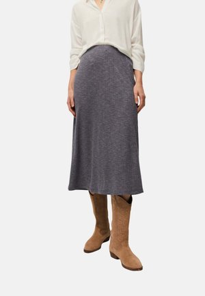 Mujer con blusa blanca, falda midi gris acanalada y botas altas de ante color camel con tacones bajos, de pie frente a un fondo liso.