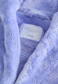 Vêtement de nuit en polaire violet clair, avec une texture douce et une étiquette portant l'inscription "NIGHTWEAR by NEXT", fabriqué en Chine.