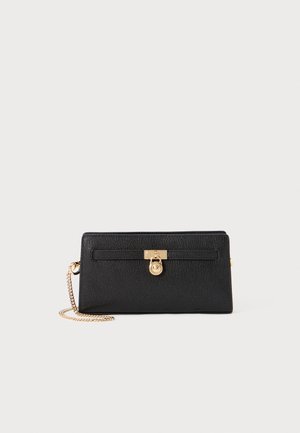 Pochette en cuir noir texturé avec bandoulière en chaîne dorée et petit fermoir rond doré à l'avant.