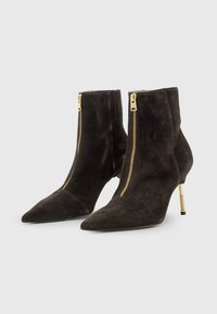 Stivaletti neri in suede, con punta affusolata, cerniere dorate sul davanti e tacchi metallici slanciati. Texture liscia e design elegante.