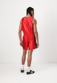 Red satin athletic tank top and shorts with black side accents, elastic waistband, and a logo on the back. Black and white shoes worn.