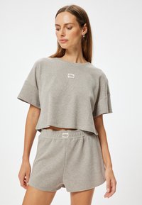 Grijze, geribbelde gebreide cropped t-shirt met korte mouwen en een klein logo. Gepaard met bijpassende grijze shorts met een elastische tailleband.