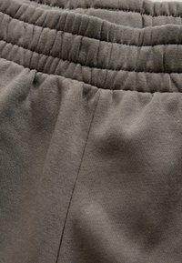 Elastīga tumši pelēka auduma materiāls ar savāktu elastīgu jostasvietu un gludu tekstūru. Aprīkots ar sānu šuves detaļu, piemērots ikdienas valkāšanai.