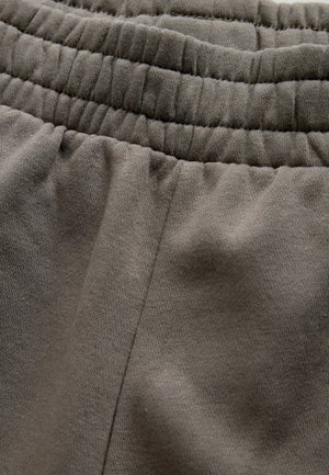 Tissu extensible gris foncé avec une taille élastique froncée et une texture lisse. Présente un détail de couture latérale, adapté pour une tenue décontractée.