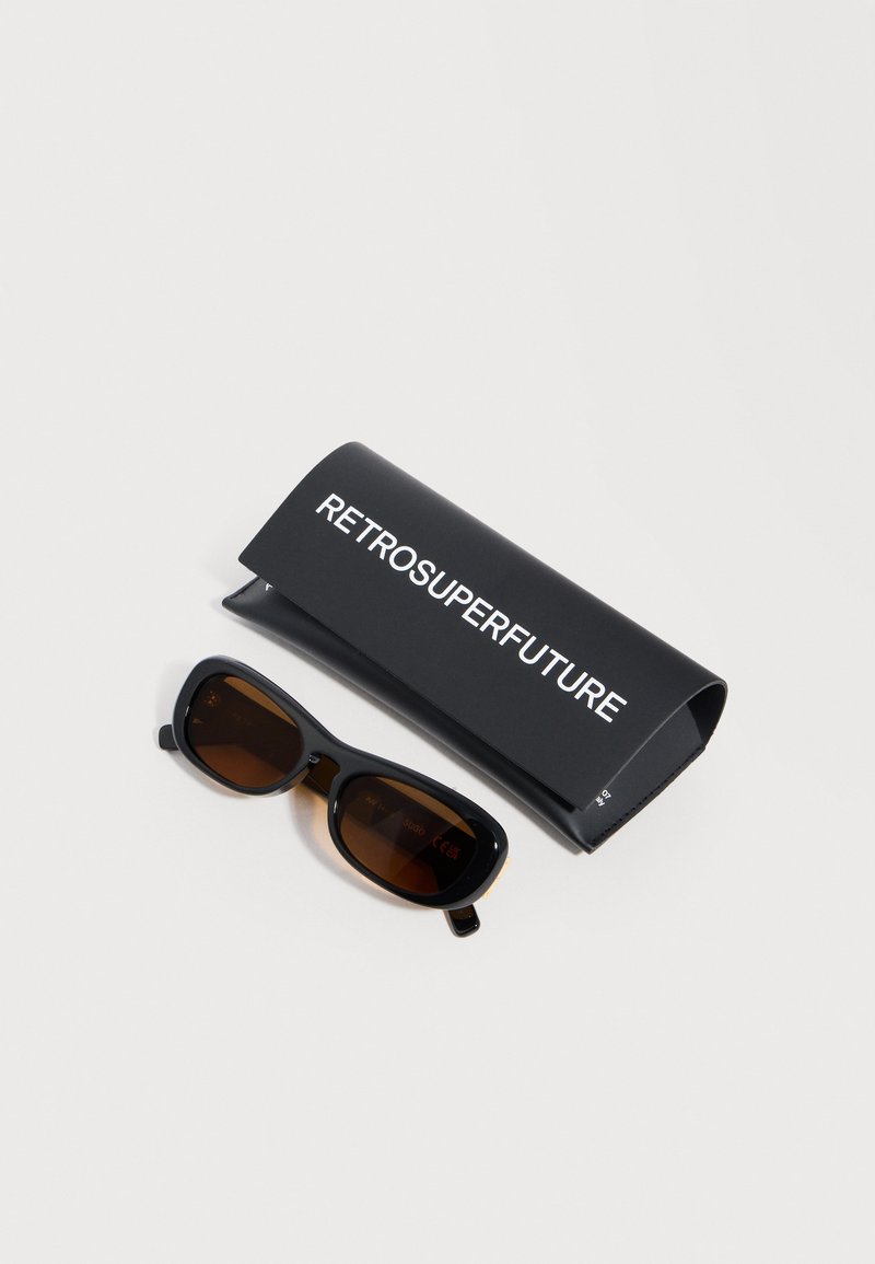 Gafas de sol rectangulares negras de estilo retro con lentes marrones, junto a un estuche negro para gafas con la etiqueta "RETROSUPERFUTURE" sobre un fondo blanco.
