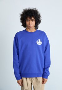 Felpa blu con scollo rotondo, polsini e orlo a coste, con un logo grafico bianco sul petto. Realizzata in tessuto testurizzato.