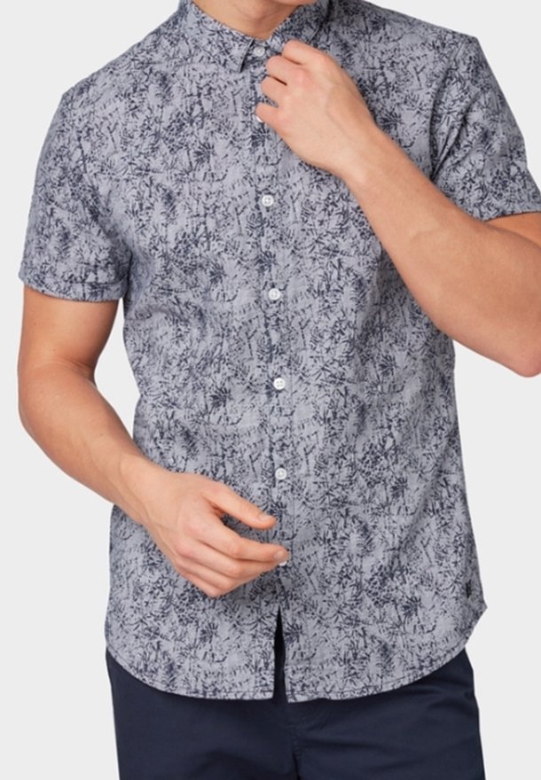 Homme portant une chemise à manches courtes boutonnée avec un motif abstrait gris et noir, ajustant le col d'une main.