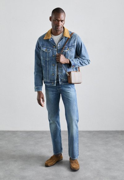 Džinsu jaka ar brūnu apkakli, gaiši zili džinsi un brūnas zamšādas kurpes. Mazs svītrains plecu maks ar ādas akcentiem.