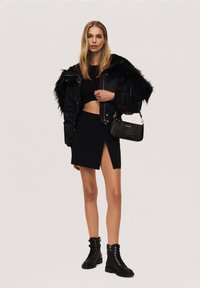 Black puffer jacket with faux fur hood, cropped black top, black mini skirt with side slit, and black lace-up ankle boots. Small black handbag.