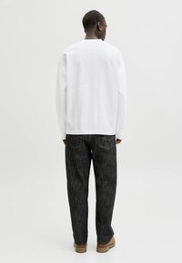 Hvid langærmet skjorte kombineret med mørkegrå denimbukser. Bukserne har kontrasterende syninger og en afslappet pasform med synlige baglommer.