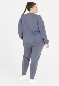Grå lounge-set i mjukt tyg. Består av en avslappnad sweatshirt med sänkta axlar och matchande tapered byxor med sidodragband.