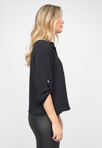 Schwarzes, leichtes Oberteil mit rundem Ausschnitt, dreiviertel Ärmeln und hochgekrempelten Bündchen. Es zeichnet sich durch eine lockere Passform und eine glatte Textur aus.