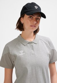 Grå pikétröja med ljusgrå detaljer och en logotyp på bröstet. Svart keps med en logotyp framtill. Kortärmad, klassisk krage.