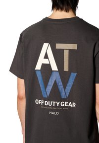 Svart bomulls t-shirt med stora, flerfärgade grafiker: "ATW" i beige och blått samt "OFF DUTY GEAR" i vitt, med en avslappnad passform.