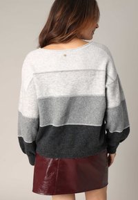 Pull rayé gris et noir, à la coupe ample, fabriqué dans un matériau doux, avec un col dégagé et des détails de couture décorative.