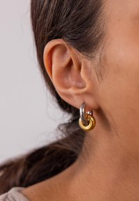 Ohrringe mit Gold- und Silberton in Form von großen, kreisförmigen Designs mit ineinander verschlungenen Ringen, glatter Textur und polierter Oberfläche.