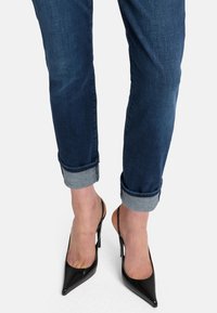 Jeans skinny blu scuro con risvolti abbinati a décolleté sling-back in pelle nera lucida, con punta affusolata e tacco a stiletto.
