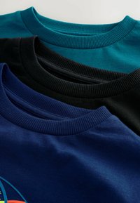 Drei Rundhals-T-Shirts aus teal, navy und schwarzer Baumwolle. Sie verfügen über gerippte Ausschnitte und glatte Texturen und werden übereinander präsentiert.