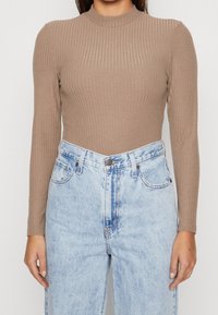 Brown ribbed long-sleeve top with a high neckline, paired with light blue high-waisted denim jeans featuring a button front and pockets.