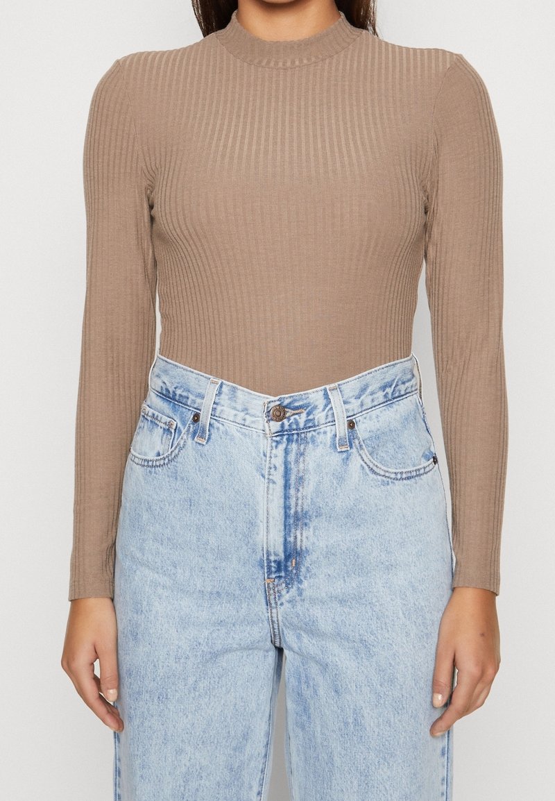 Brown ribbed long-sleeve top with a high neckline, paired with light blue high-waisted denim jeans featuring a button front and pockets.