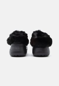 Zwarte Crocs met een zachte bontkraag. Het lichaam heeft een gladde afwerking, terwijl de zool stevig is met een gestructureerd grip patroon.