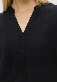 Top nero con scollatura a V, tessuto testurizzato con dettagli a leggero motivo e piega frontale. Materiale morbido e leggero.