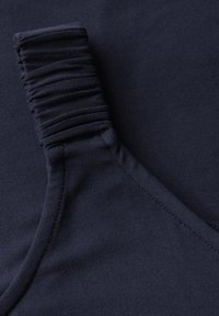 Un primo piano di un tessuto blu navy presenta un dettaglio elastico arricciato lungo il bordo, con una texture liscia e una leggera lucentezza. Le linee delle cuciture sono visibili.