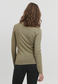 Olivgrön tröja med långa ärmar, figursydd design, rundad halsringning och ribbad nederkant. Mjuk stickad textur. Bärs med svarta byxor.