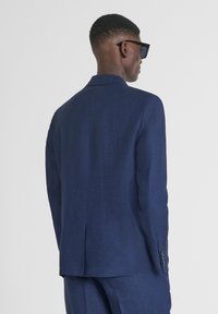 Blazer azul marino hecho de tejido texturizado, con una abertura en la parte posterior, un diseño ajustado y detalles de botones minimalistas en las mangas.