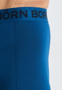 Boxer breve blu senza giunture con una vita marchiata nera, caratterizzato da una texture liscia e un design aderente, che mette in evidenza la moderna costruzione dei capi.