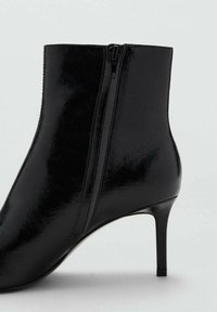 Bottine en cuir noir avec une finition brillante, bout pointu et fermeture éclair sur le côté. Présente un talon aiguille fin et une texture lisse.
